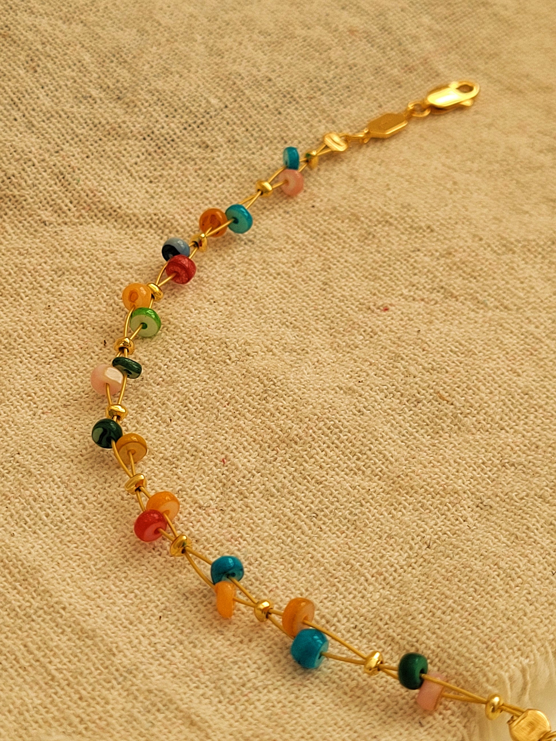 Multicolored beaded bracelet on a gold chain against a beige fabric background