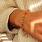 Close-up of a wrist wearing a colorful beaded bracelet against a textured beige background