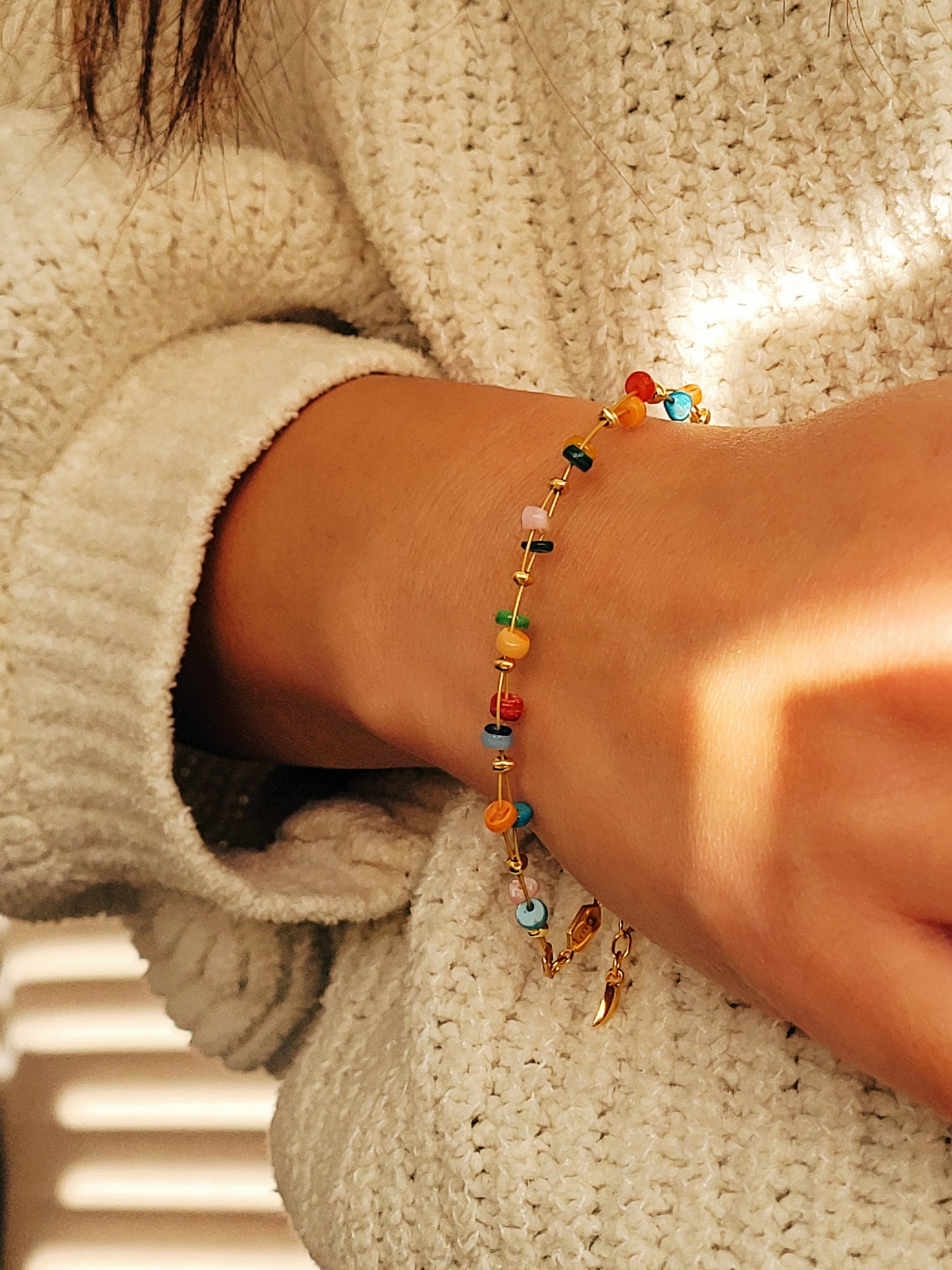 Close-up of a wrist wearing a colorful beaded bracelet against a textured beige background