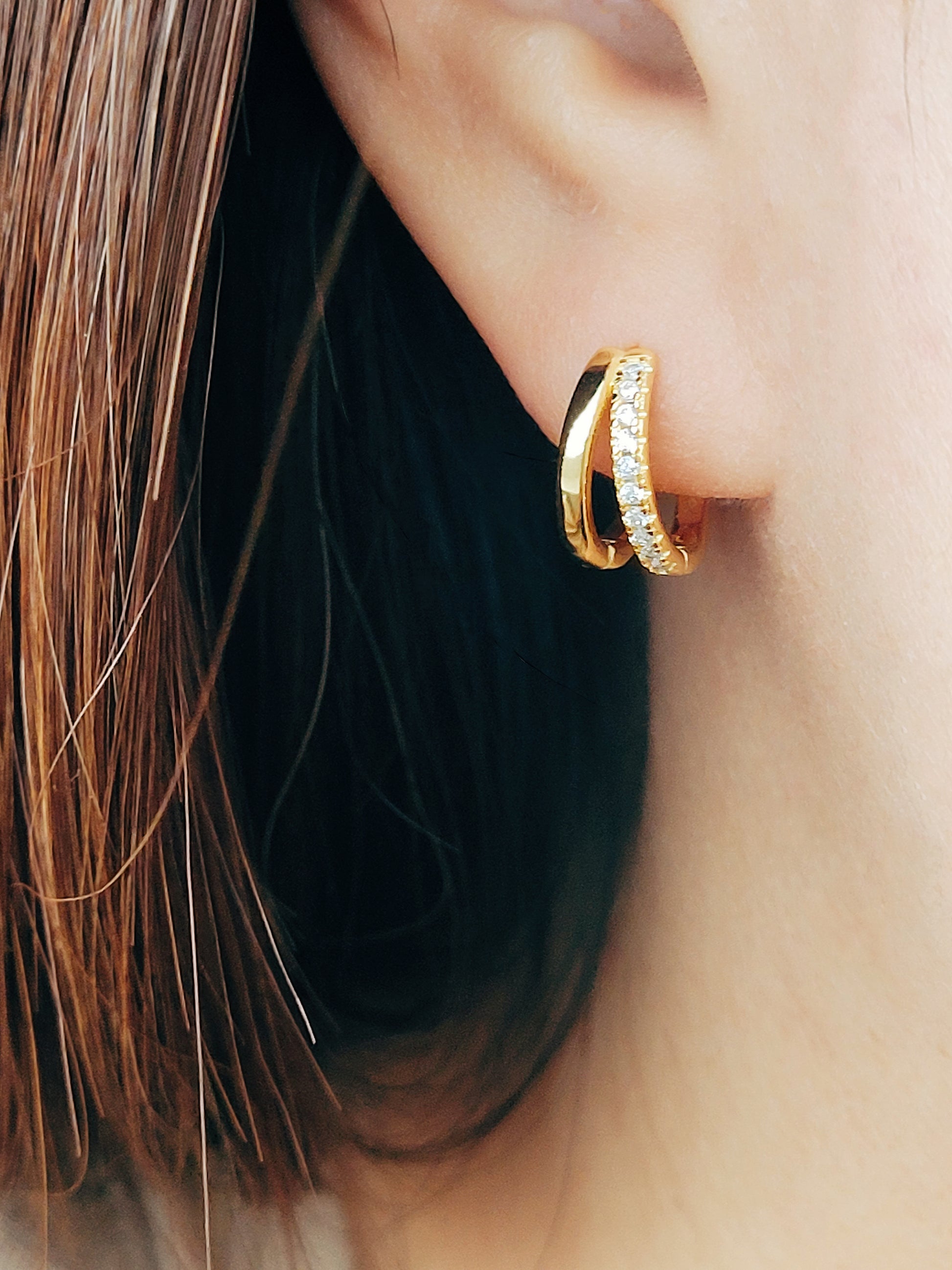 A woman wearing gold double huggie hoop, designed to hug the earlobe for a chic and modern look.