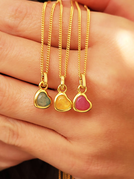 Three gold necklaces with heart-shaped gemstones crafted in 18k gold vermeil and crystal quartz held in a hand.