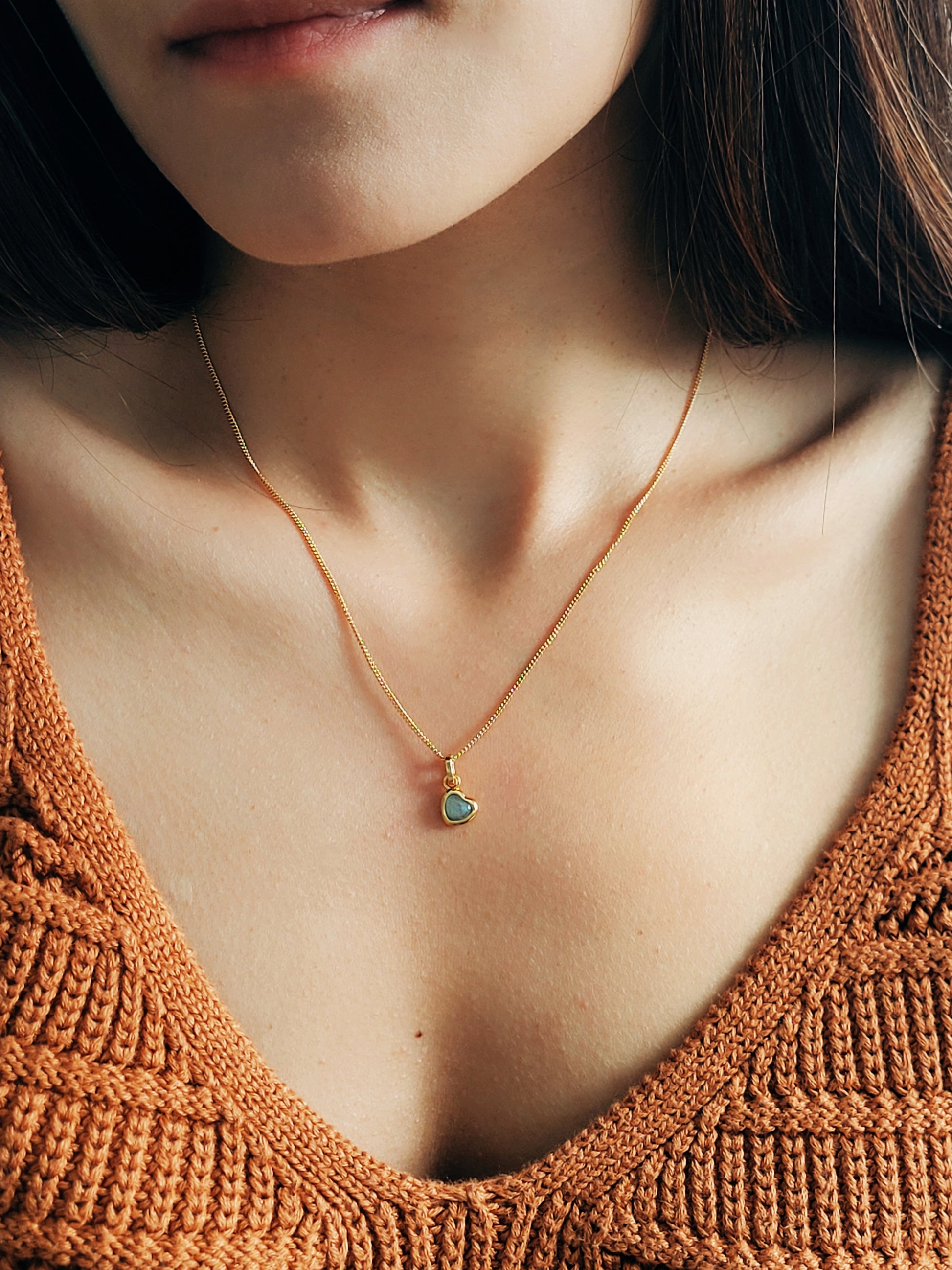 Close-up of a woman wearing a gold heart necklace with a green crystal quartz pendant, elegant and romantic