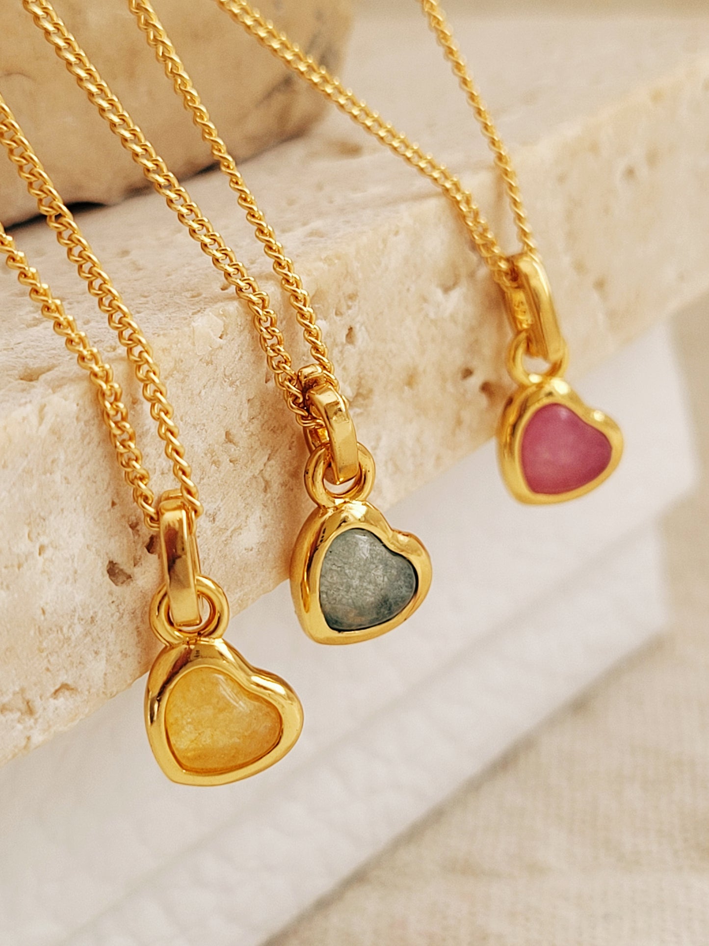 Gold heart-shaped pendants with embedded gemstone in yellow, green and pink.