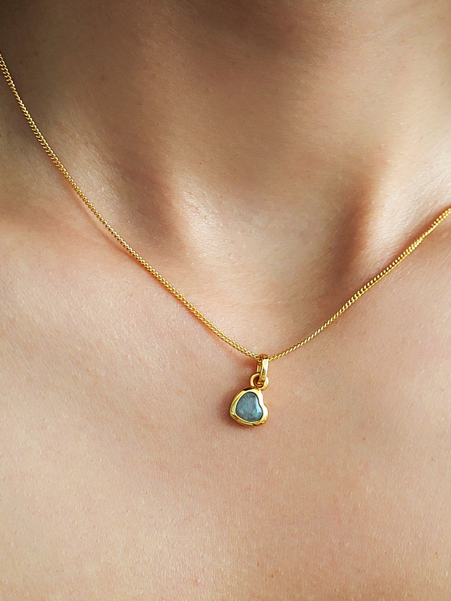 Gold necklace with a heart gemstone pendant on a woman's neck.