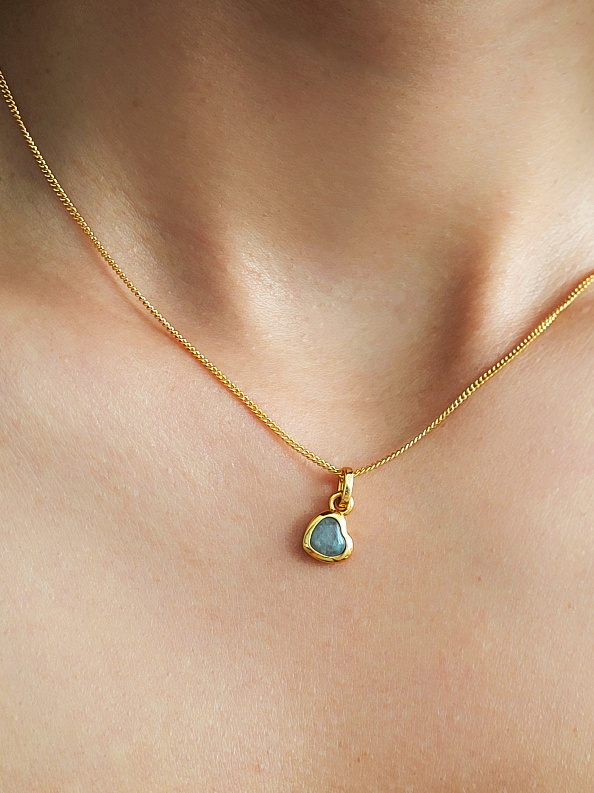 Gold necklace with a heart gemstone pendant on a woman's neck.