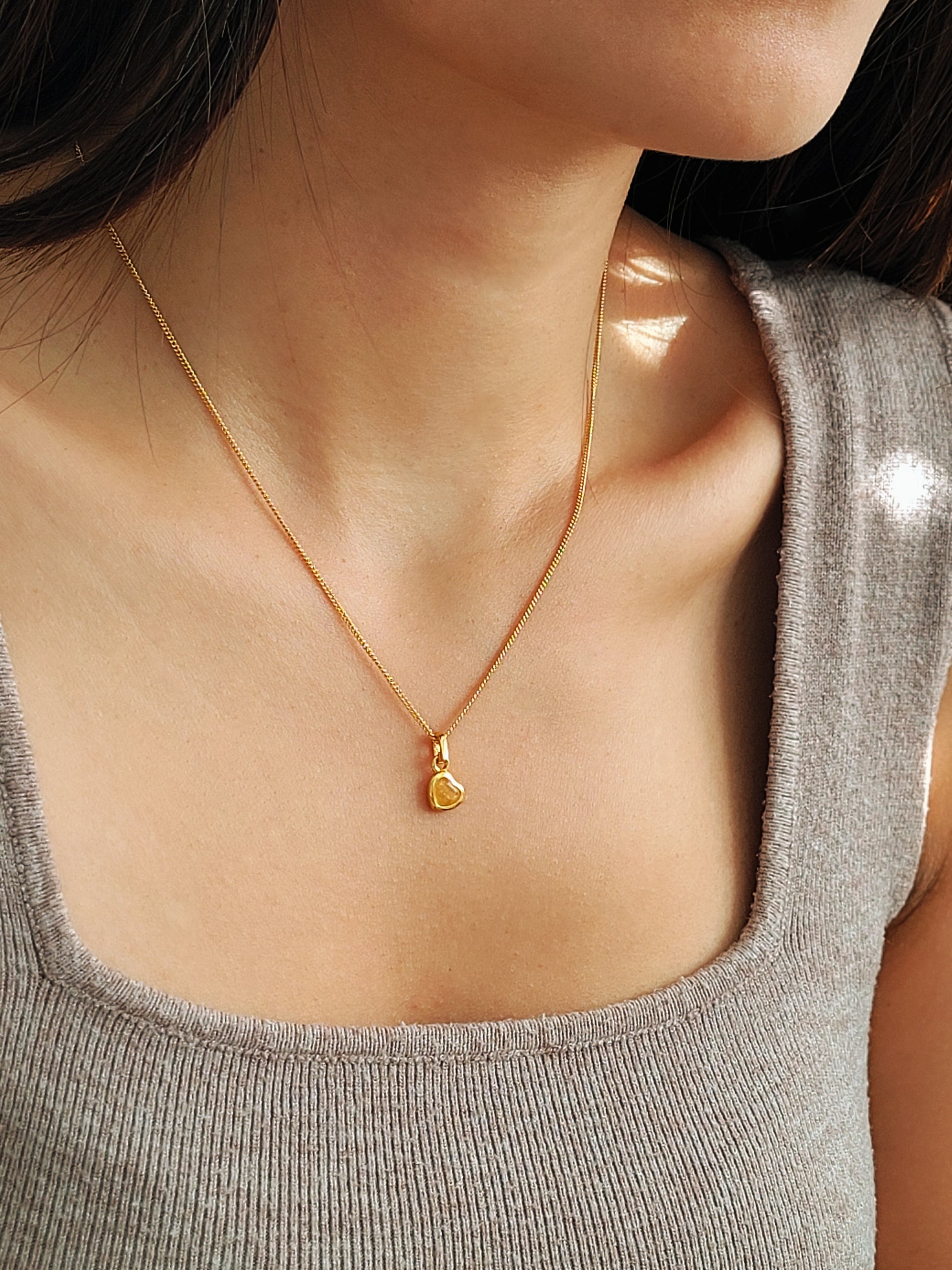 Gold heart necklace with a heart pendant worn by a girl in a gray tank top.