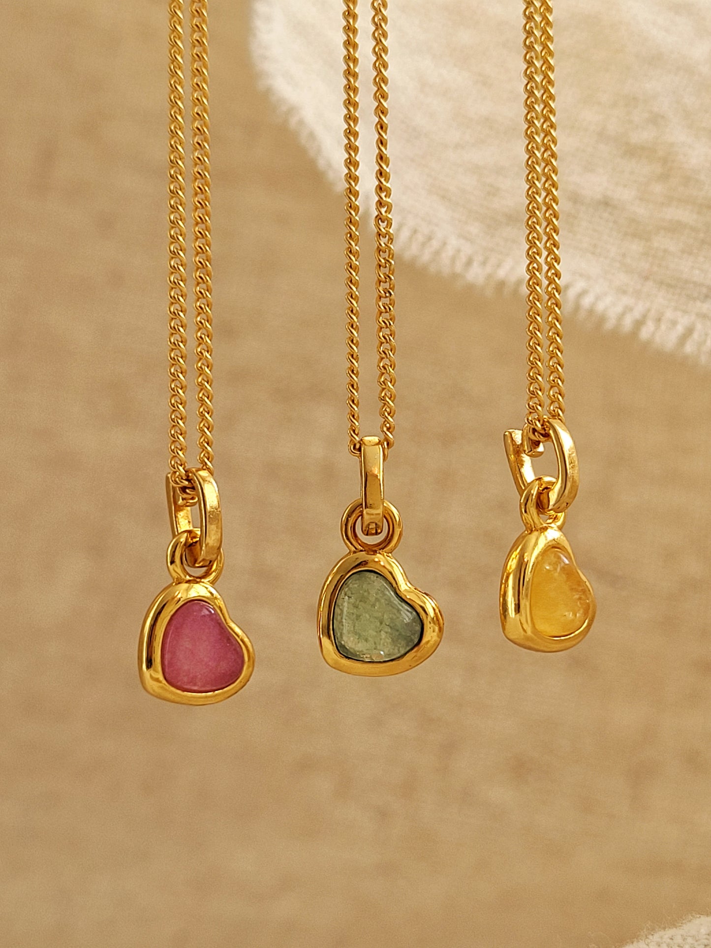 Three gold necklaces with heart-shaped gemstones on a beige background