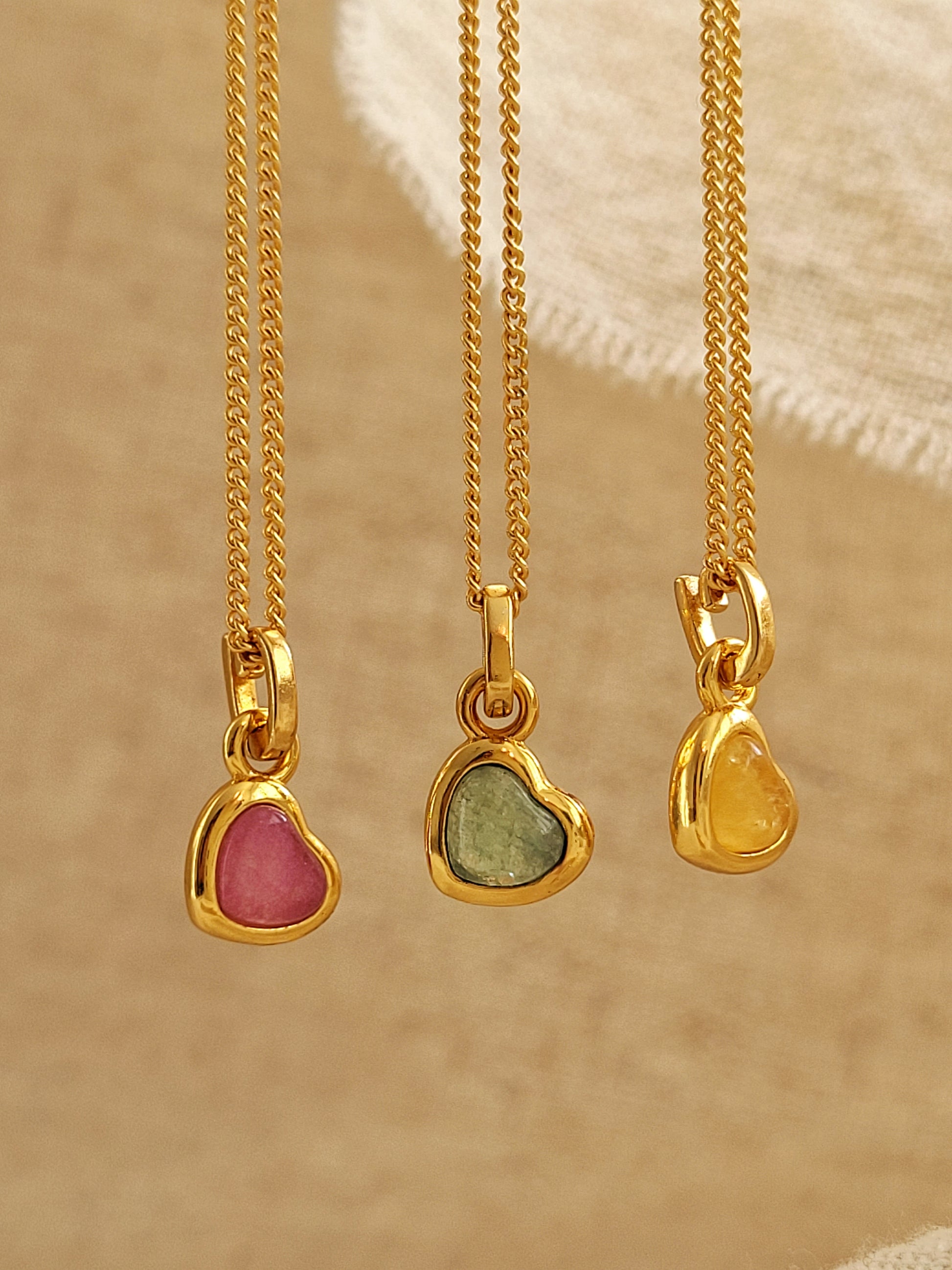 Three gold necklaces with heart-shaped gemstones on a beige background