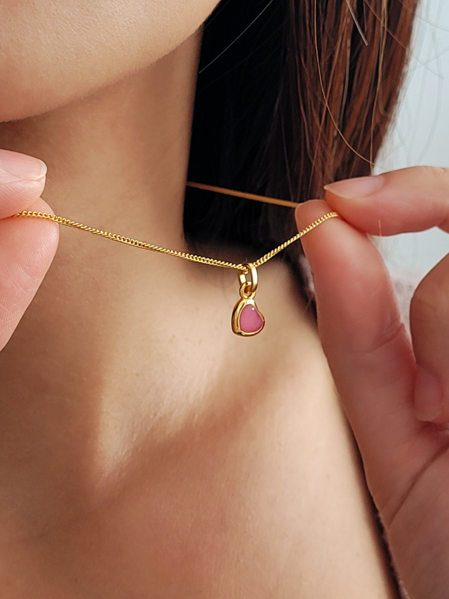 Gold necklace with a pink heart pendant being worn on a girl.
