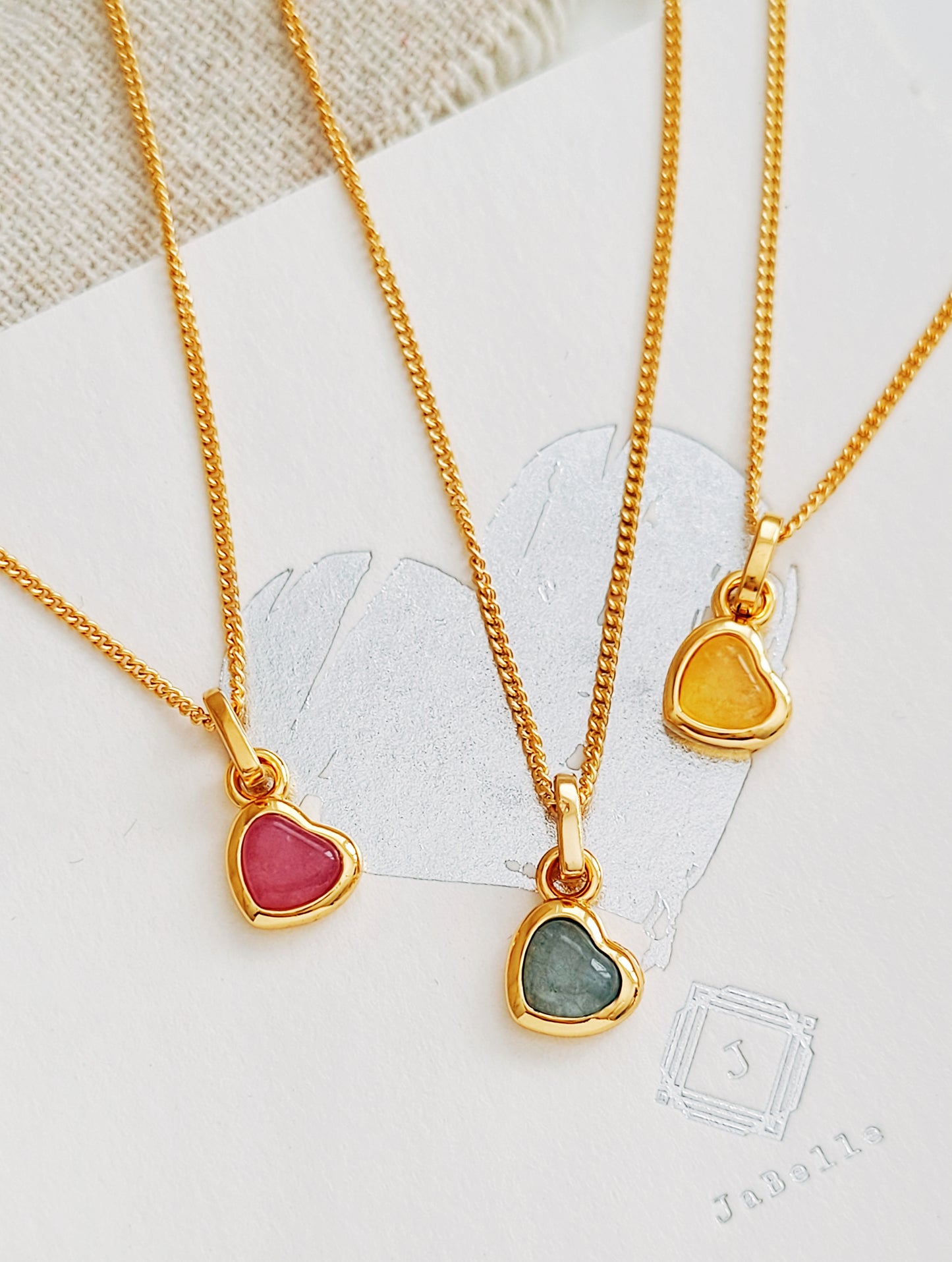 Three gold necklaces with heart-shaped gemstones on a white background