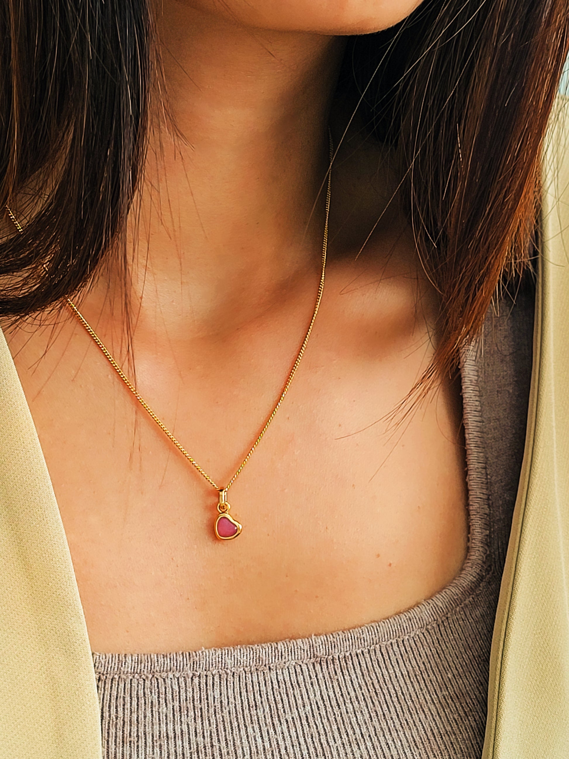 Gold necklace with a heart-shaped pendant worn by a person