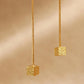 Close-up of two gold box chain threader earrings showing the fine detail of the textured, glittering square cube charms suspended at the ends against a warm, neutral background.