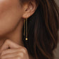 A woman with dark hair wearing a single gold box chain threader earring with a small geometric cube charm hanging elegantly below her earlobe.