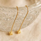 Close-up of two gold box chain threader earrings showing the fine detail of the textured, glittering square cube charms suspended at the ends against a warm, neutral background.