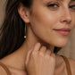 A woman with curl brown hair wearing a gold box chain threader earring pull through with a small geometric cube charm hanging elegantly below her earlobe.