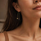 A woman with dark hair wearing a single gold box chain threader earring with a small geometric cube charm hanging elegantly below her earlobe.
