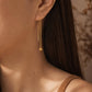 A woman with dark hair wearing a single gold box chain threader earring with a small geometric cube charm hanging elegantly below her earlobe.