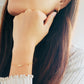 A woman highlights her adorable gold bow bracelet, blending comfort with chic style.