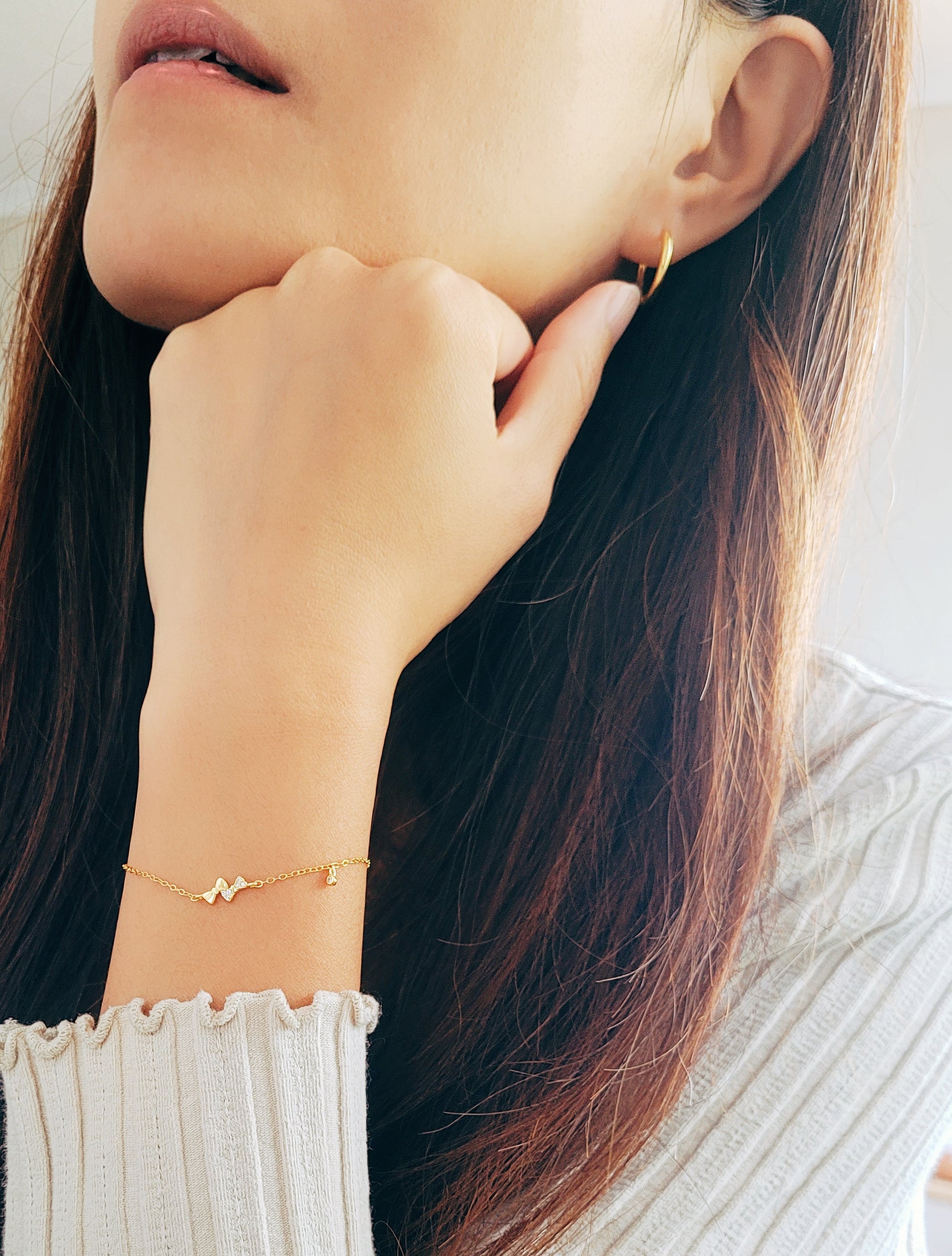 A woman highlights her adorable gold bow bracelet, blending comfort with chic style.