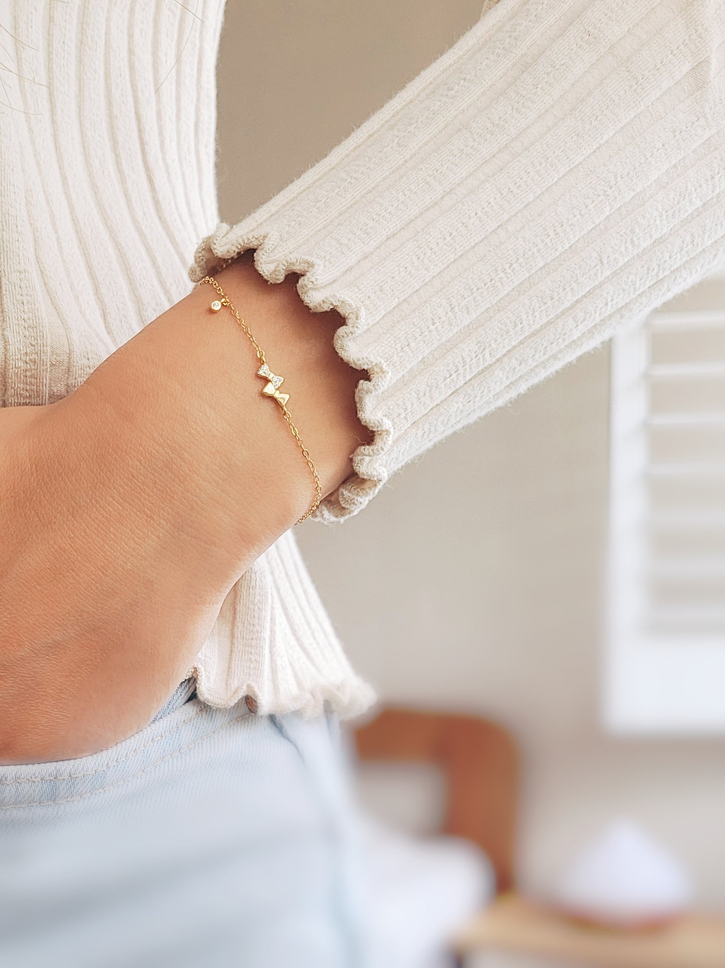 A woman in a white sweater flaunts a cute gold bow bracelet, perfectly complementing her casual yet stylish look.