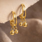 Dainty gold double hoop earrings with dangling balls on a soft beige background, everyday minimalist jewellery.