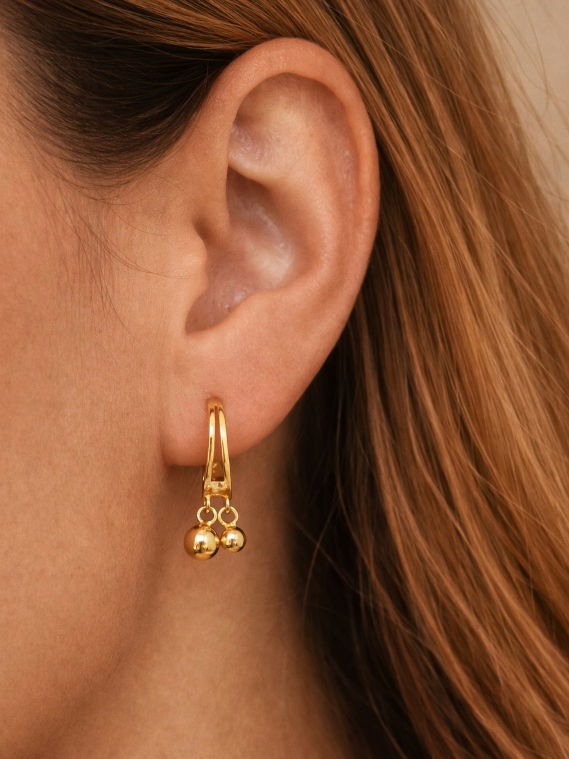 Gold double hoop earrings with small spherical charms worn by a woman, elegant and edgy earrings for everyday wear.