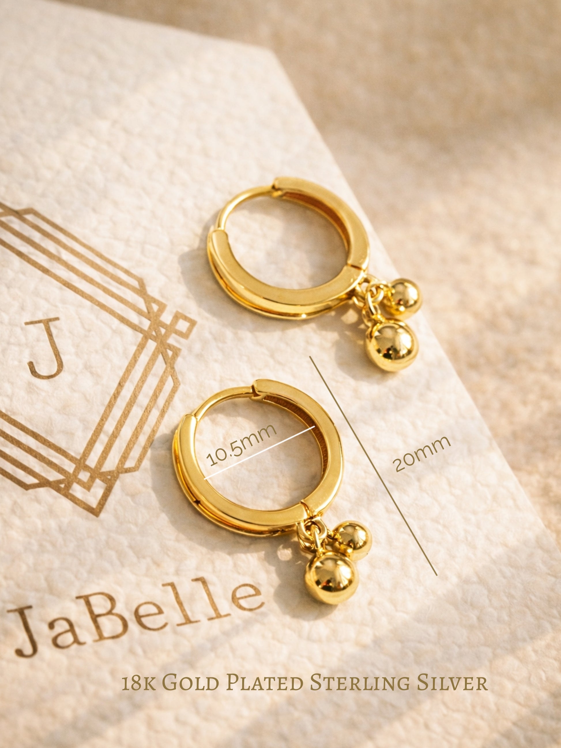 Gold hoop earrings with spherical charms on a JaBelle branded card, designed in UK.