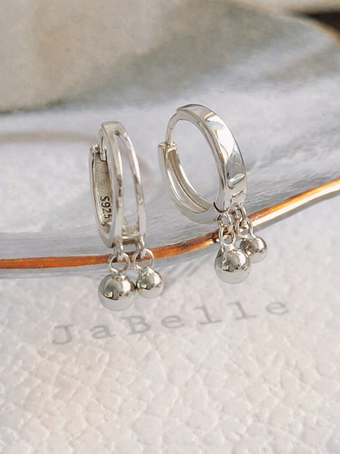 Silver double hoop earrings with small ball charms on a white surface with 'JaBelle' branding, modern and stylish earrings crafted in 925 sterling silver.