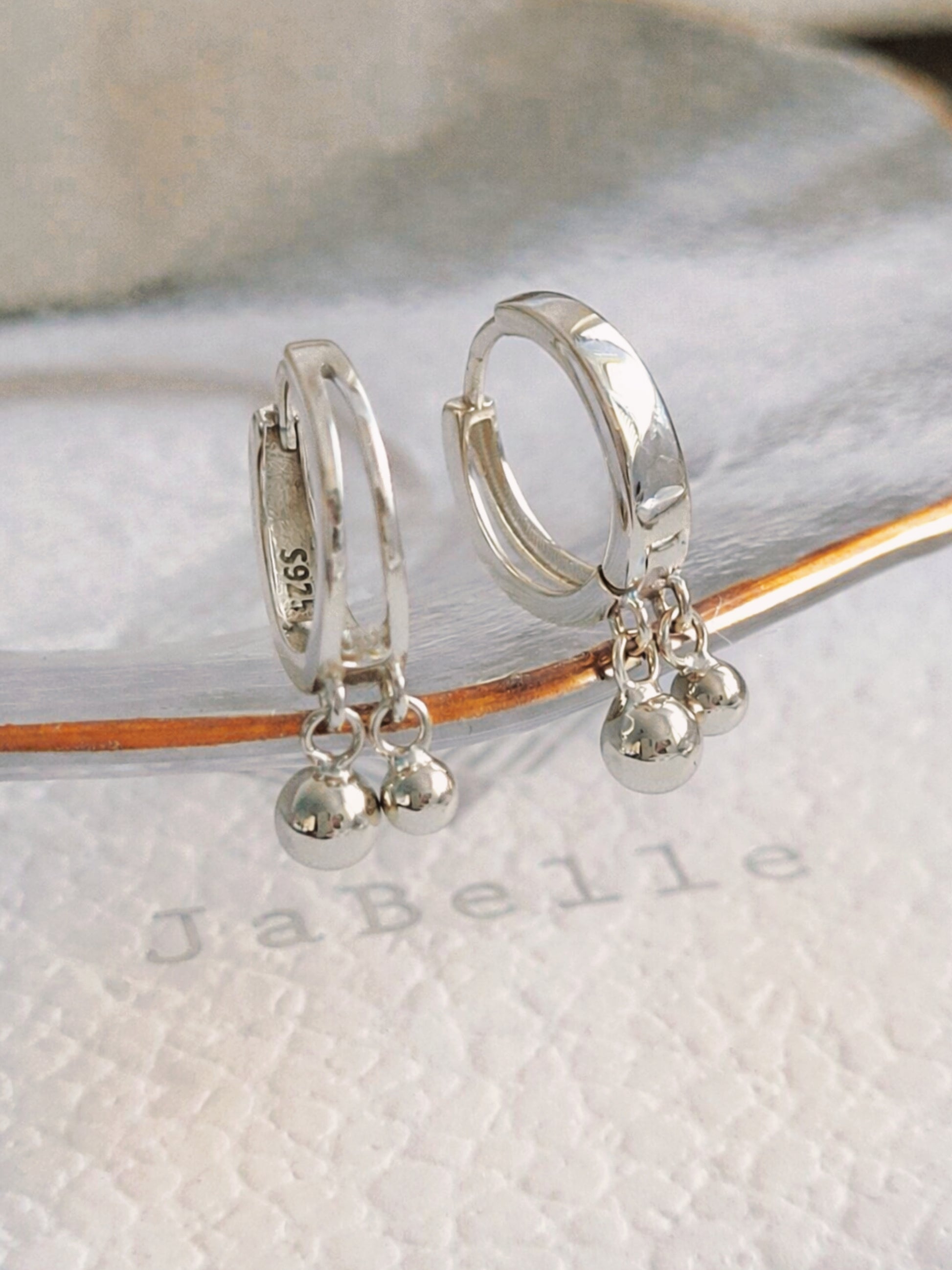 Silver double hoop earrings with small ball charms on a white surface with 'JaBelle' branding, modern and stylish earrings crafted in 925 sterling silver.