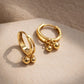Close up of a pair of gold hoop earrings with spherical charms on a beige surface, crafted in gold plated sterling silver, waterproof and hypoallergenic. 