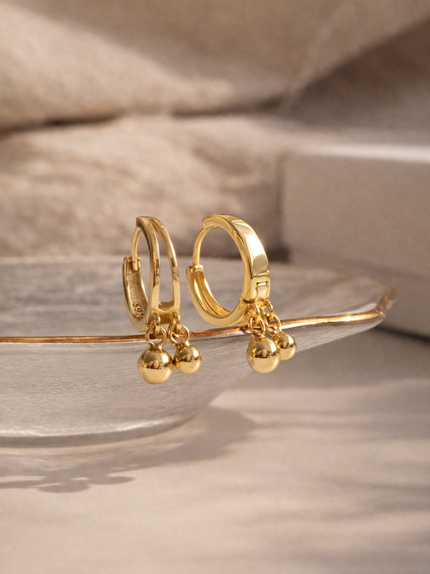 Gold hoop earrings with small spherical charms on a neutral background