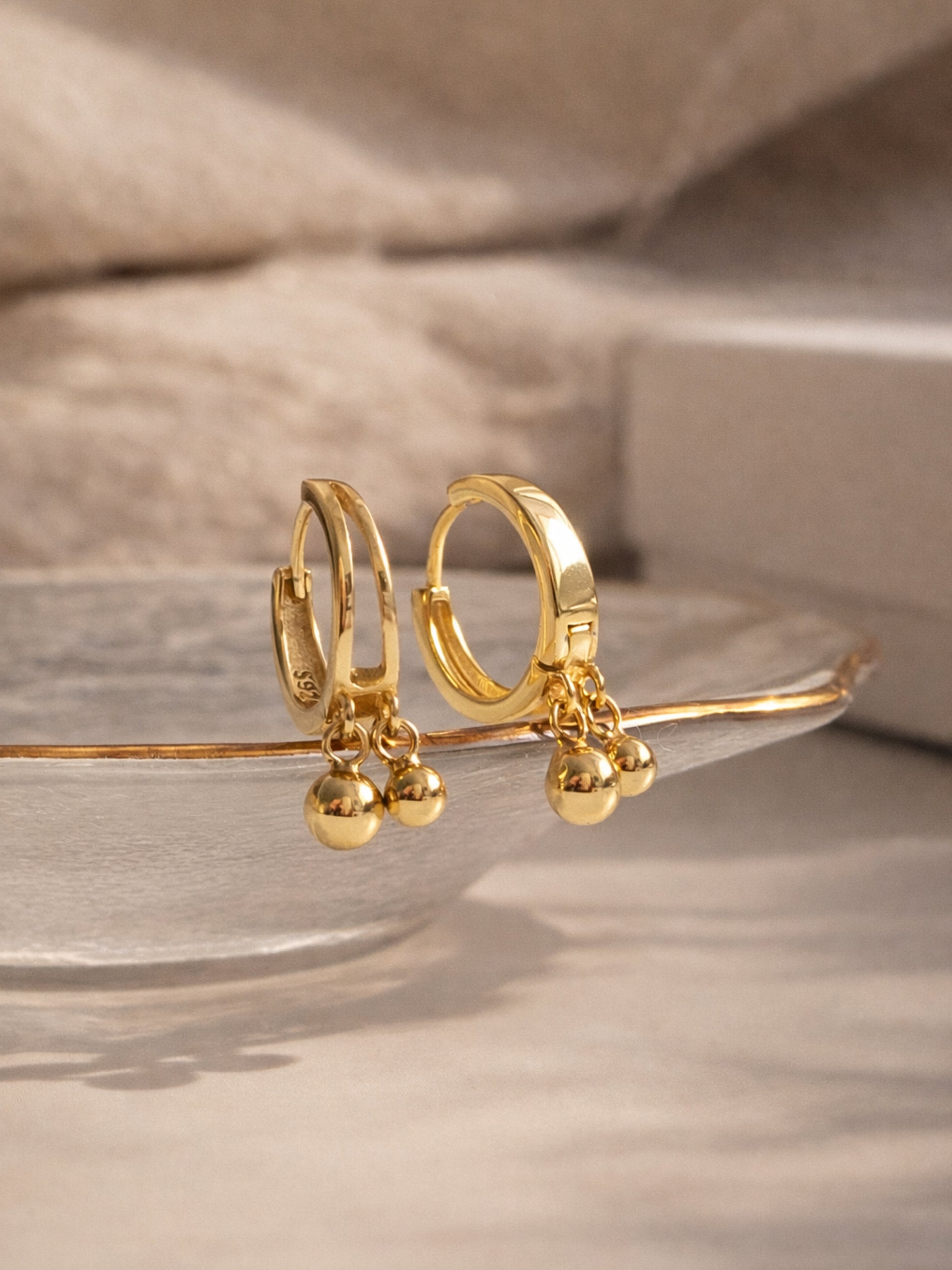 Gold hoop earrings with small spherical charms on a neutral background