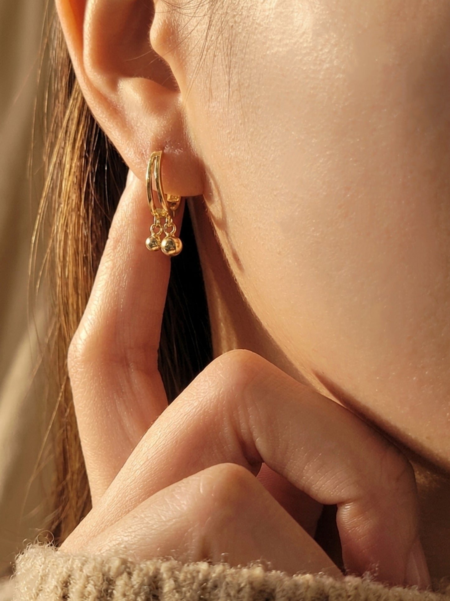 Close-up of a woman wearing gold hoop earrings with small ball charms dangle, dainty jewellery gift for her.