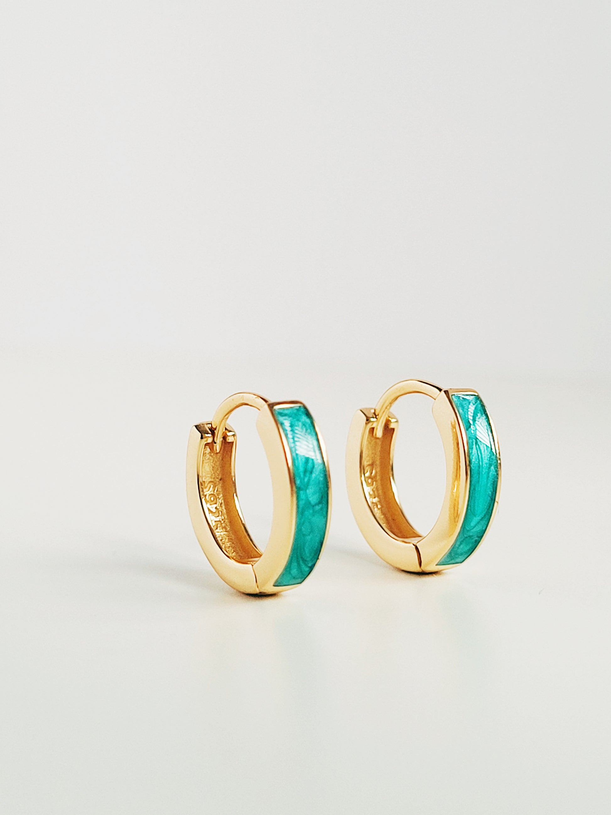 A stunning pair of gold and turquoise enamel huggie hoop earrings, perfect for adding a pop of color to any outfit.