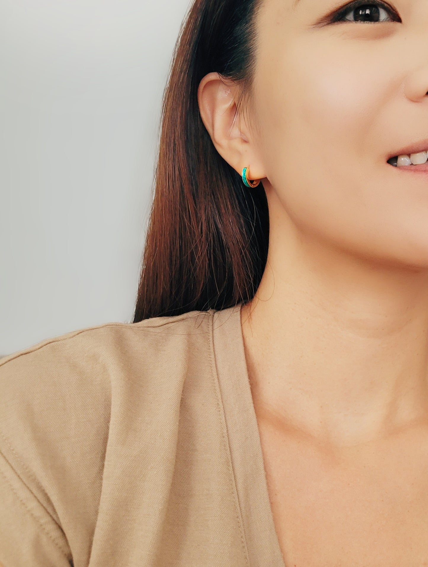 Smiling woman flaunting her colorful Enamel Huggie Hoop earrings, radiating joy and style.