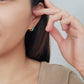 A woman models colorful enamel huggie hoop earrings, each in a different hue, adding a playful touch to her outfit.