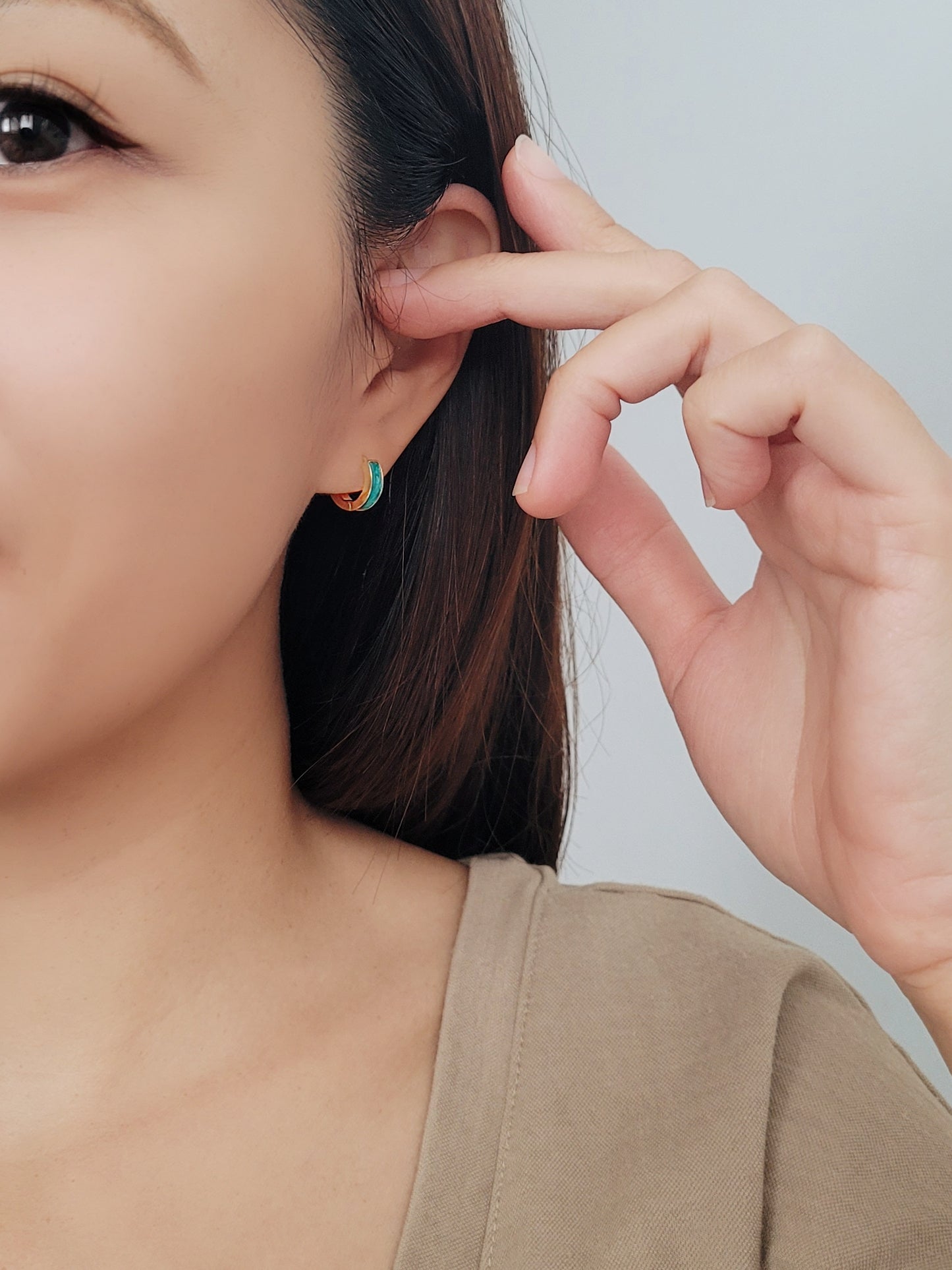 A woman models colorful enamel huggie hoop earrings, each in a different hue, adding a playful touch to her outfit.