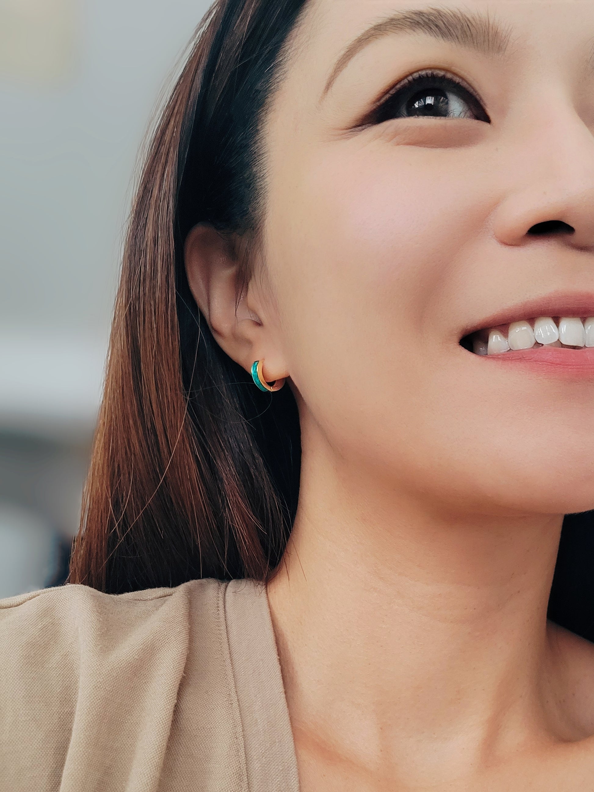 A woman smiles brightly, showcasing her stylish Enamel Huggie Hoop earrings.