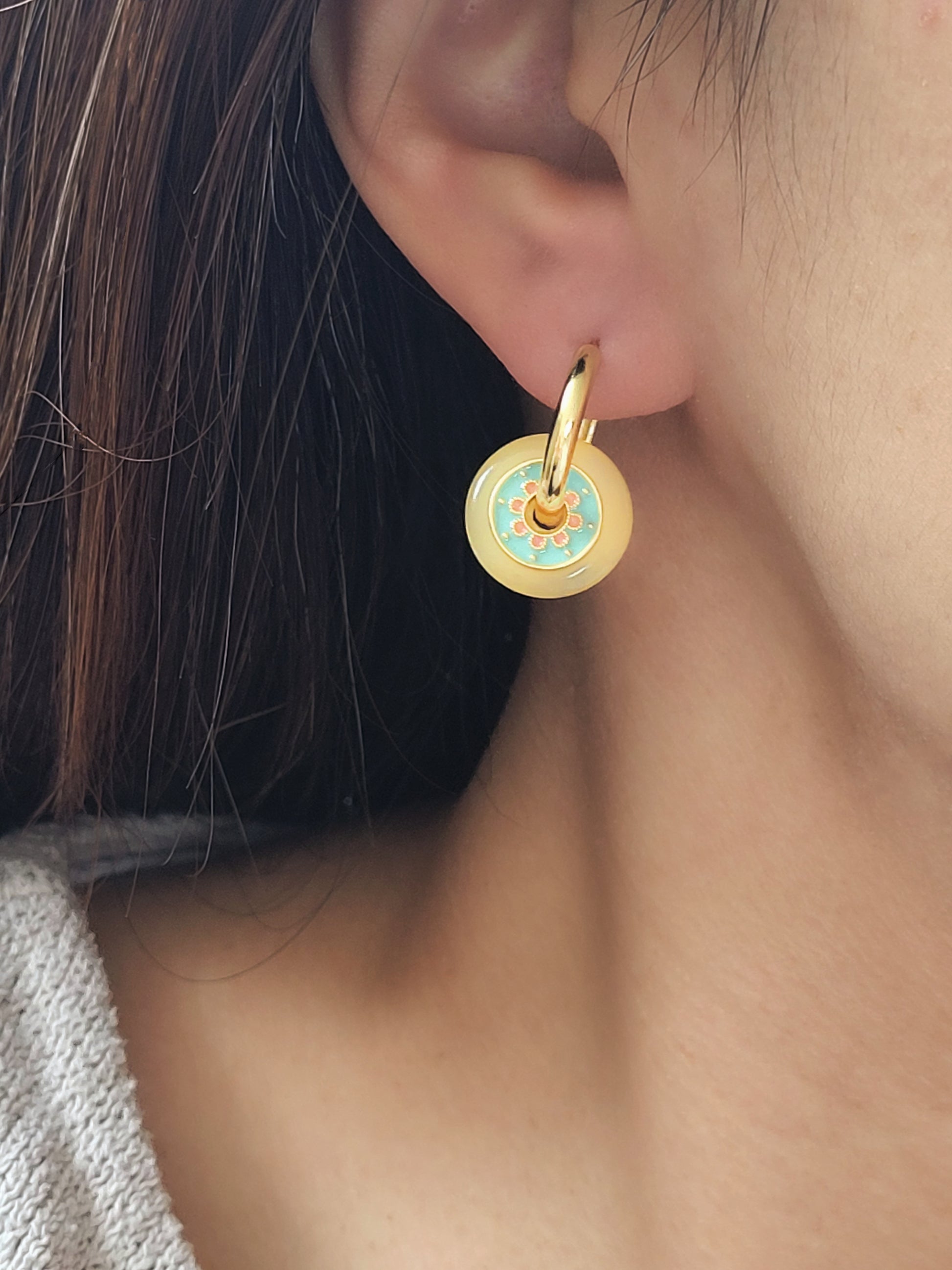 A woman wearing a yellow glass drop earrings with intricate enamel details and vintage-inspired style.