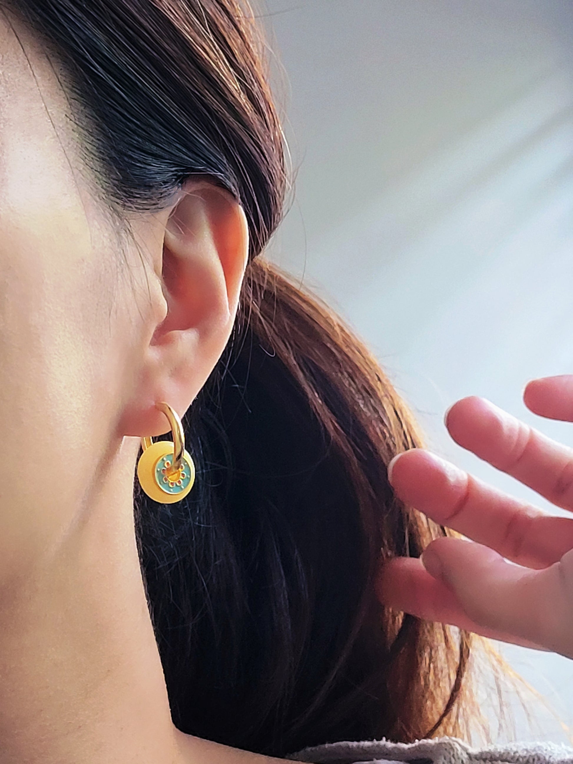 Close up of a woman wearing vintage-inspired enamel disc earrings with yellow glass drop and gold-plated hoops.