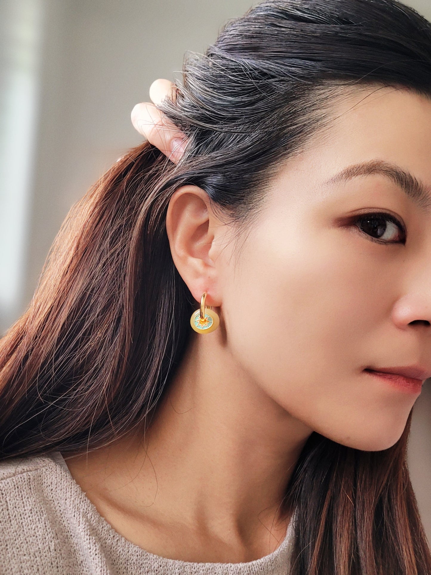 Close up of a woman wearing vintage-inspired enamel disc earrings with yellow glass drop and gold-plated hoops.