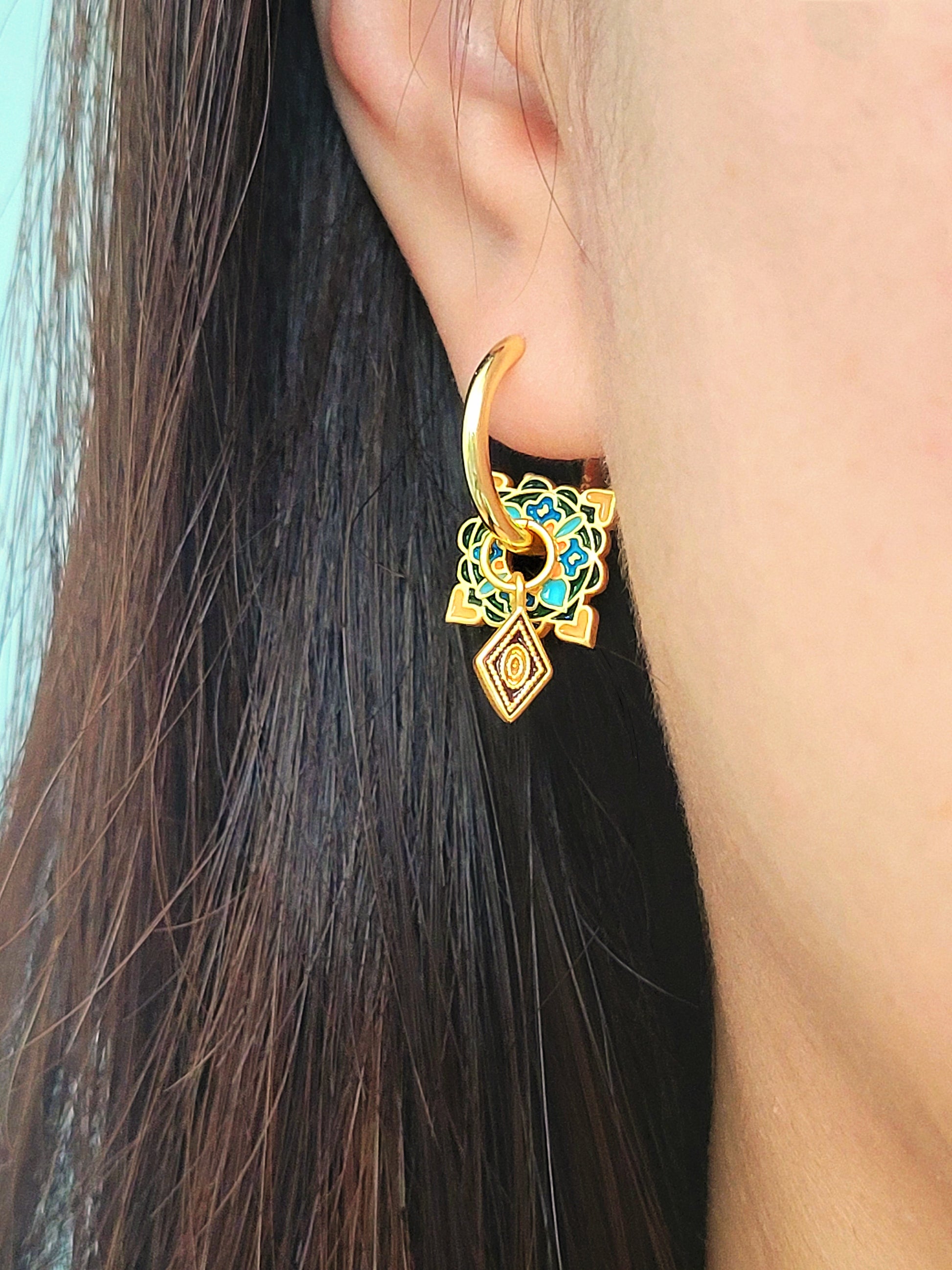 Close-up of elegant tile-inspired Enamel hoop earrings with vibrant geometric enamel designs and gold accents on a woman's ear.