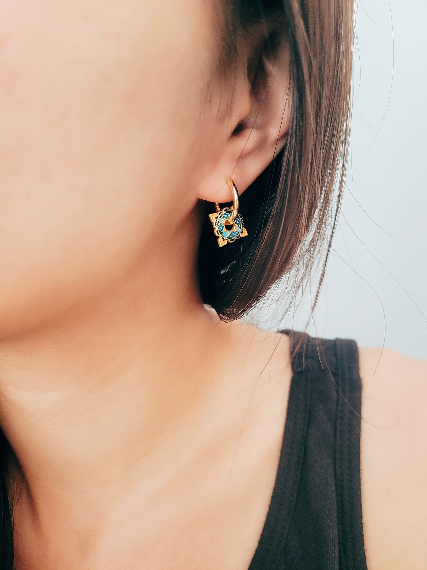 Close-up of elegant tile-inspired Enamel hoop earrings with vibrant geometric enamel designs and gold accents on a woman's ear.