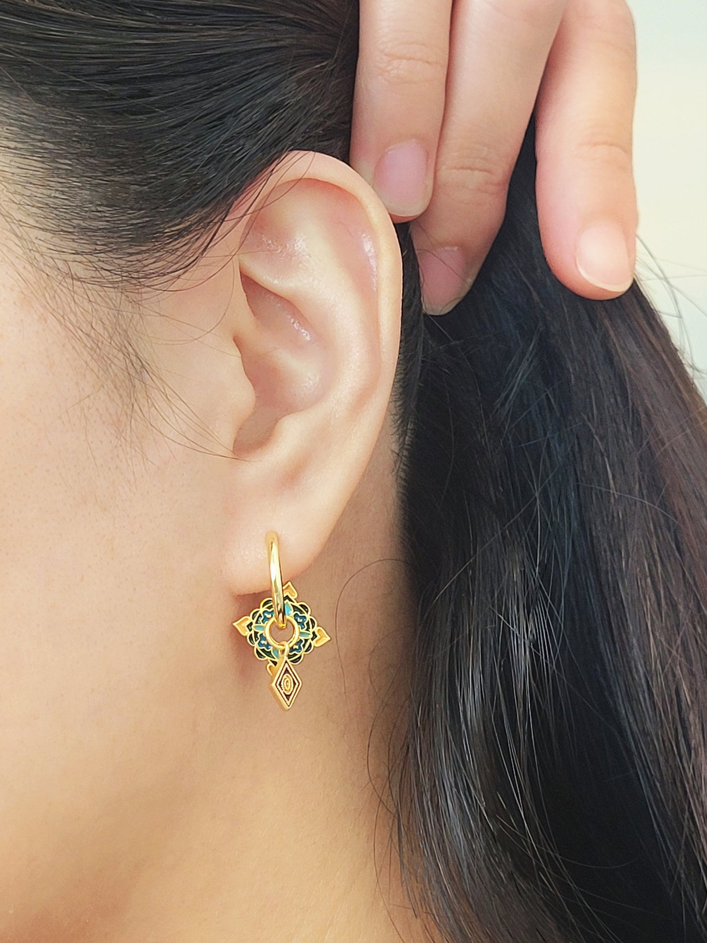 Close-up of elegant tile-inspired Enamel hoop earrings with vibrant geometric enamel designs and gold accents on a woman's ear.