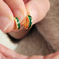Gold and green earrings held between fingers against a neutral background