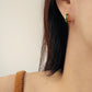 Close-up of an ear wearing a gold huggie hoop earring with green enamel on a neutral background