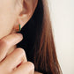 Close-up of a woman wearing a gold earring with a green enamel wave pattern