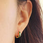Close-up of an ear wearing a gold hoop earring with green enamel