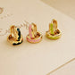Three small gold hoop earrings with colorful enameled designs on a beige surface in dark green, pink and lime colors.