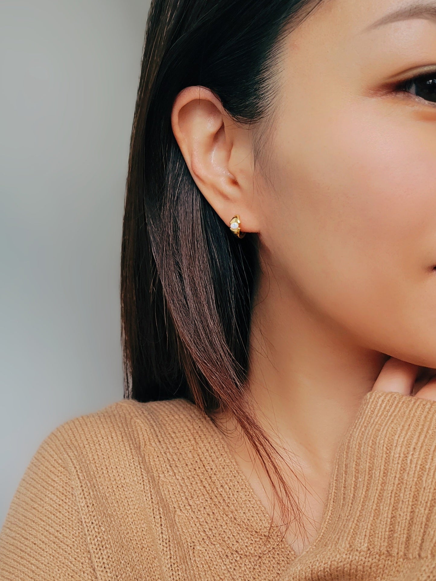 A woman wearing gold-plated sterling silver evil eye opal huggie earrings with a dainty minimalist design. 
